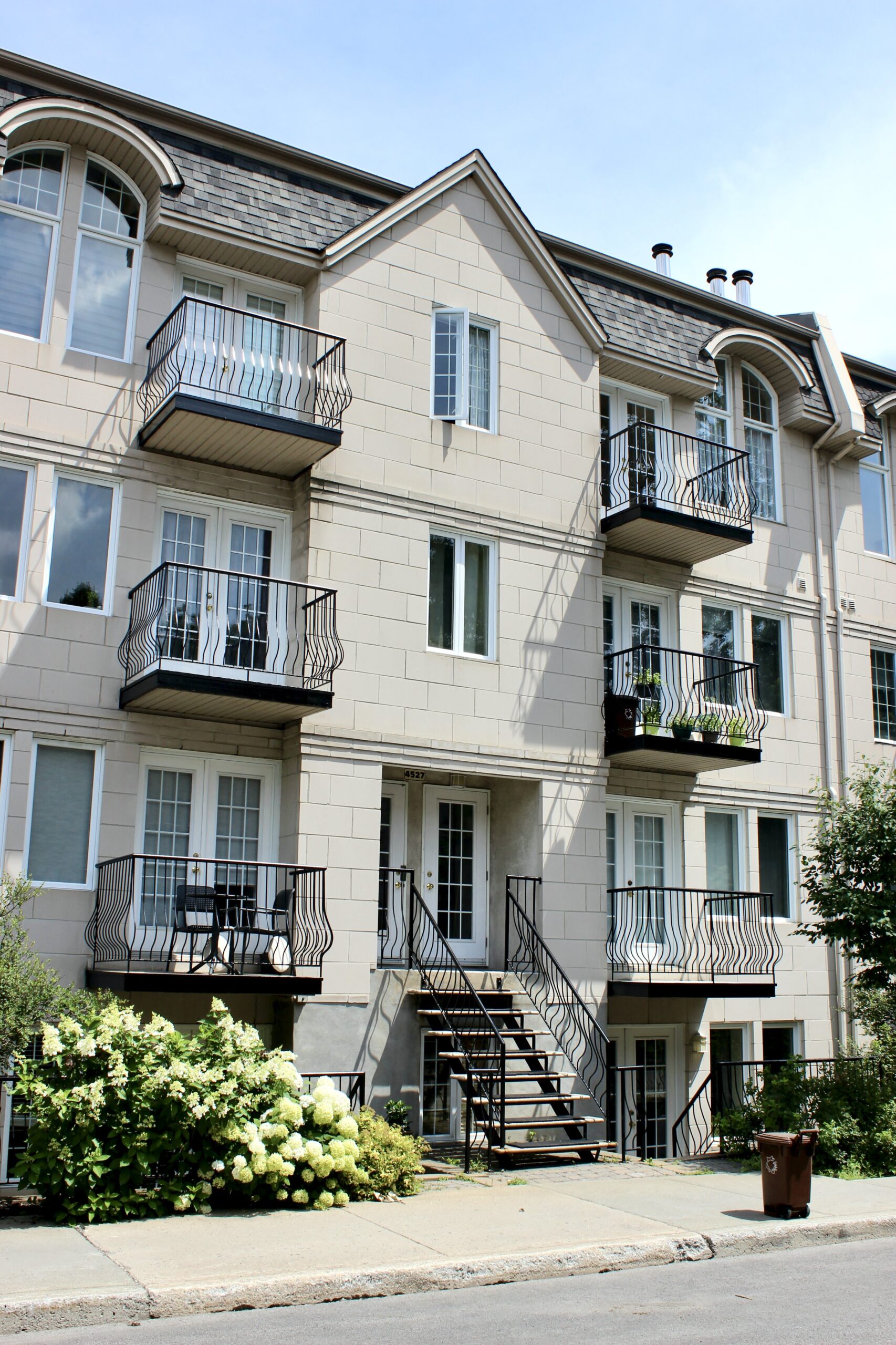 Immeuble résidentiel avec balcons en fer forgé noir et façade claire, typique d’un bâtiment à logements au Québec